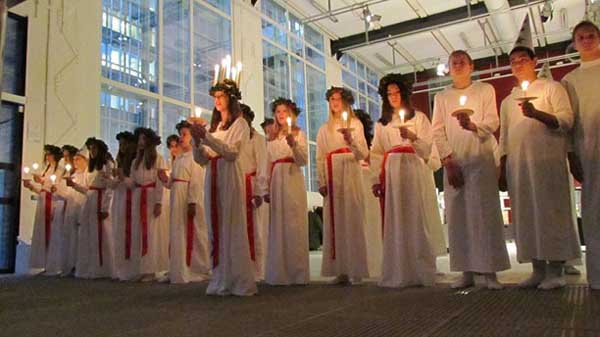 En esta imagen se aprecia las chicas con sus vestidos blancos y el fajín rojo y Santa Lucia destaca con su corona de velas. En tanto, los chicos se ven con sus vestidos con capirotes.